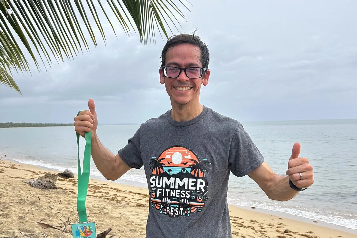 Giomarell en la playa con una medalla de carrera, levantando el pulgar