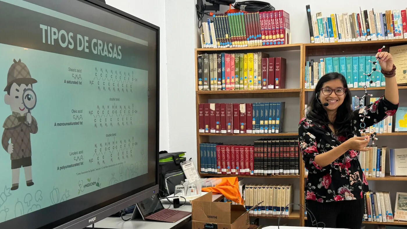 Dr. Chelsea presenting 'Tipos de Grasas' with a molecular model at a community workshop